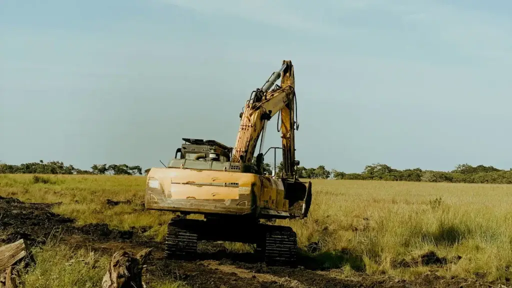 Tracked excavator crossing soft ground on a rural land-clearing site