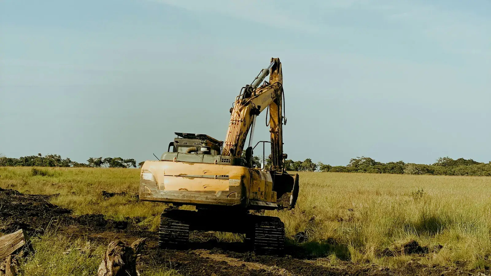Tracked excavator crossing soft ground on a rural land-clearing site
